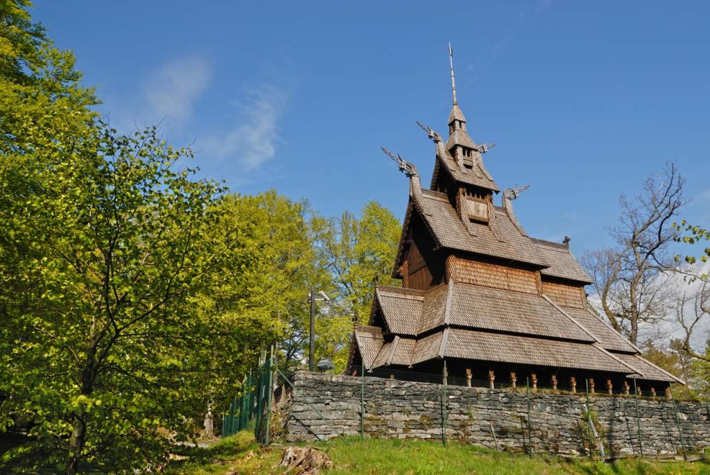 Fantoft Stavkirke med grønn skog og blå himmel.